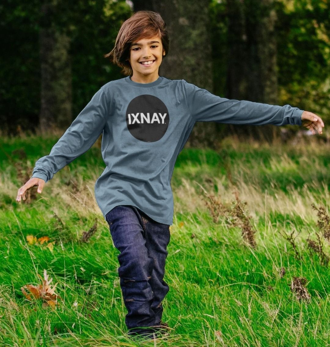 Boy playing in field while wearing a kids stone blue organic long-sleeved t-shirt with original black round IXNAY logo