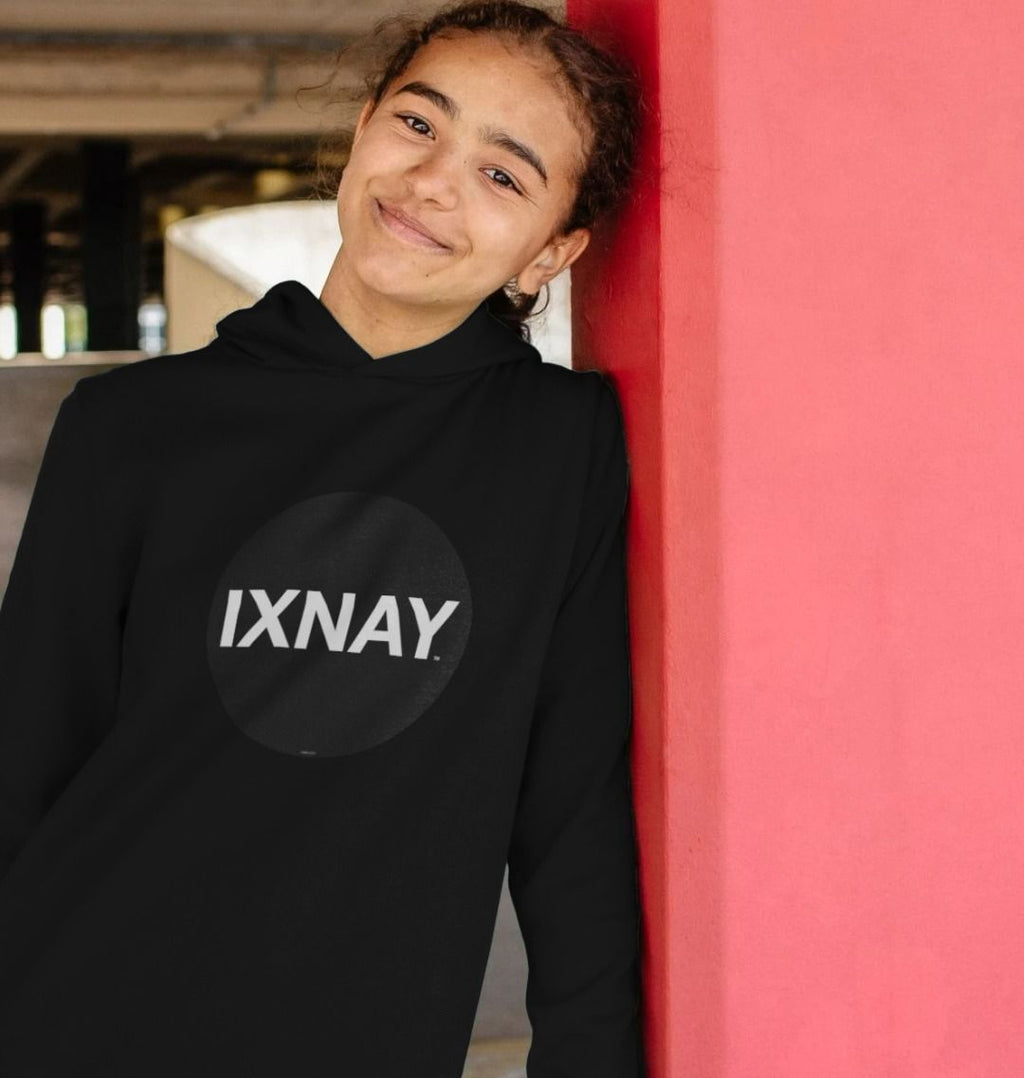Girl leaning against red column in a car park wearing kids black organic relaxed fit pullover hoodie with original black round IXNAY logo