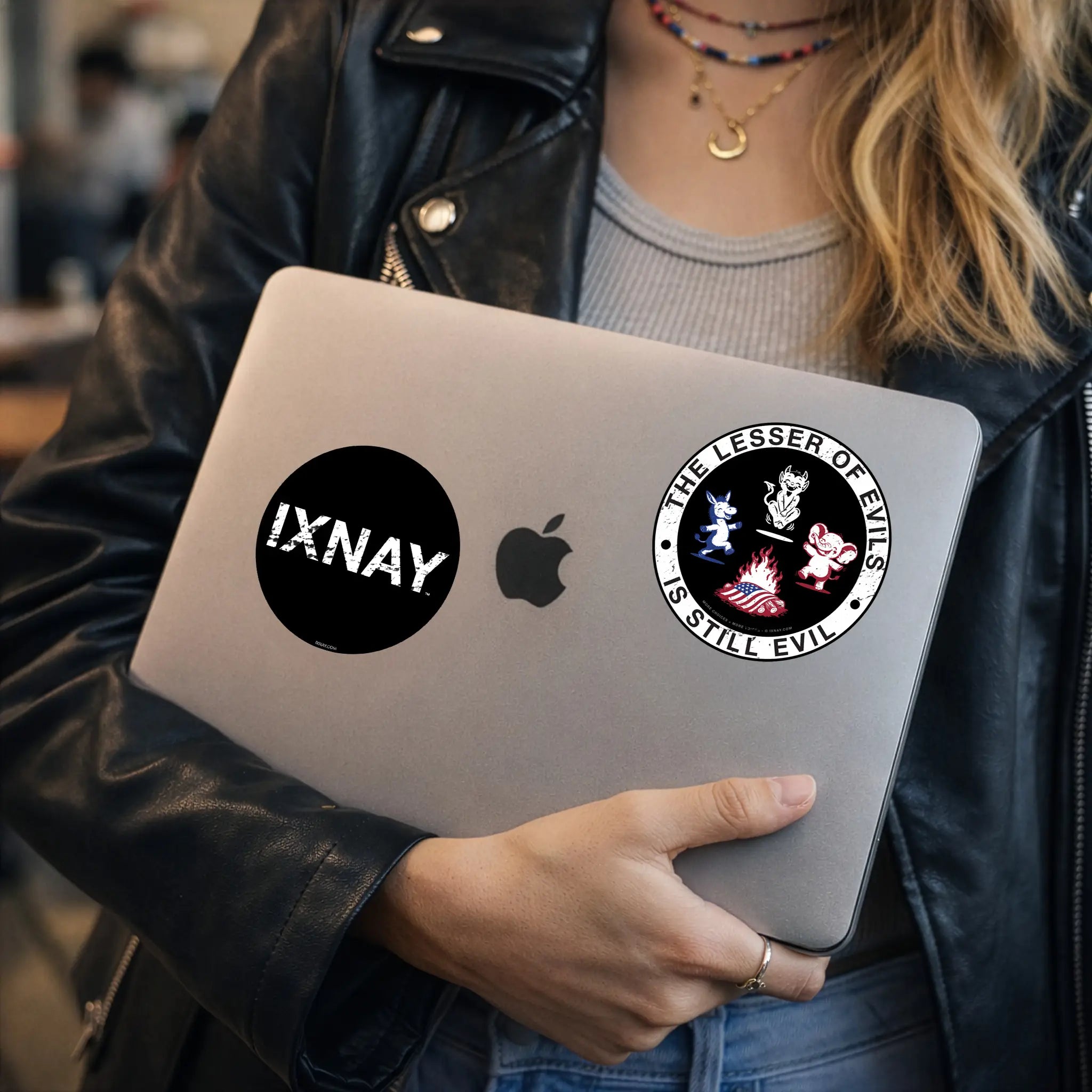 Woman carrying a laptop with an IXNAY political graphic with donkey, elephant, and devil figure around a campfire with an American flag, labeled 'The Lesser of Evils is Still Evil' on an adhesive paper sticker.