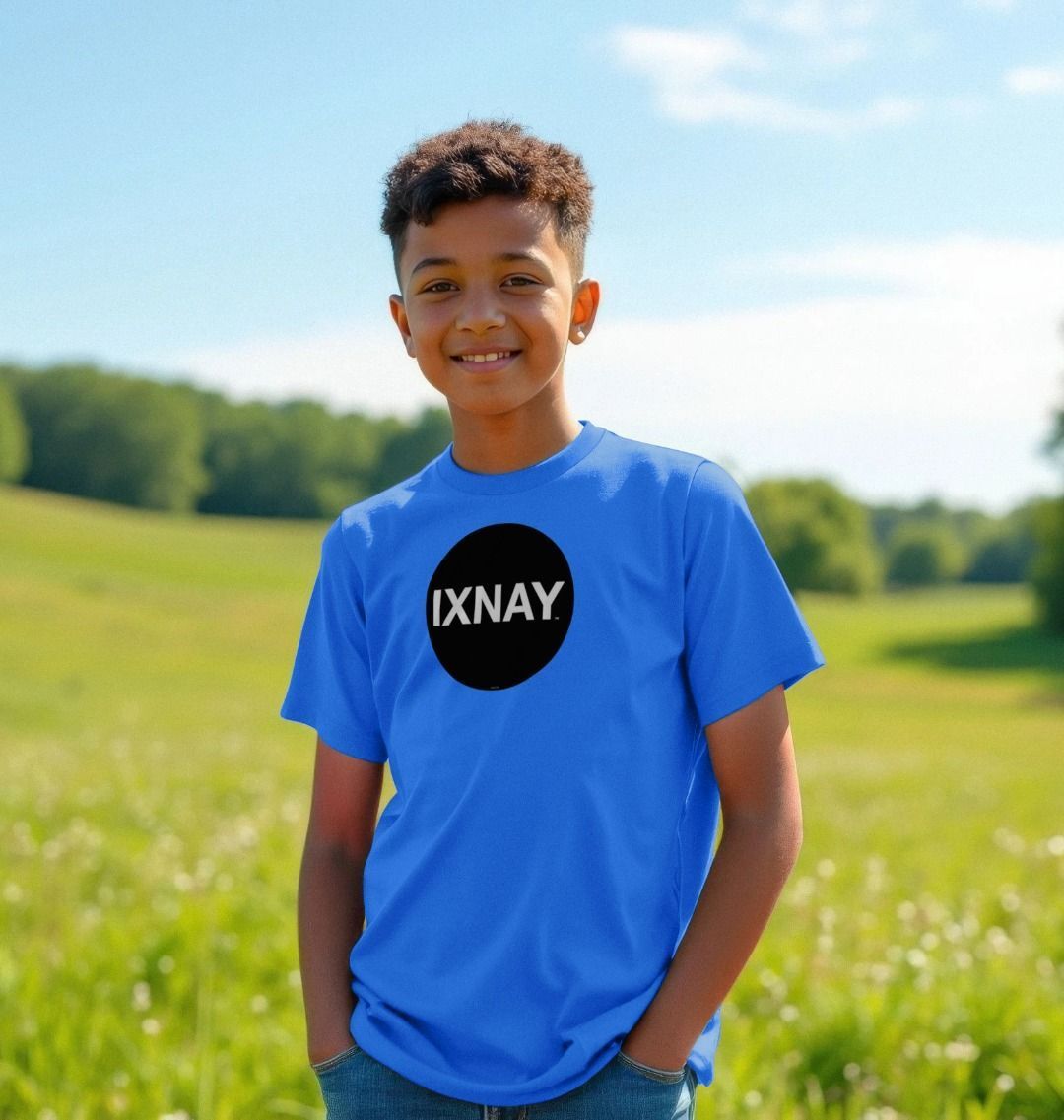 Smiling boy in a sunlit green field wearing a bright blue t-shirt with the original IXNAY black circular logo printed on the front