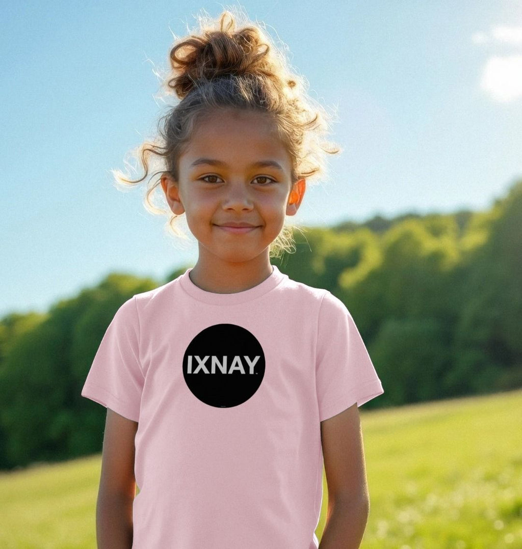 Smiling girl in a sunlit green field wearing a light pink t-shirt with the original IXNAY black circular logo printed on the front