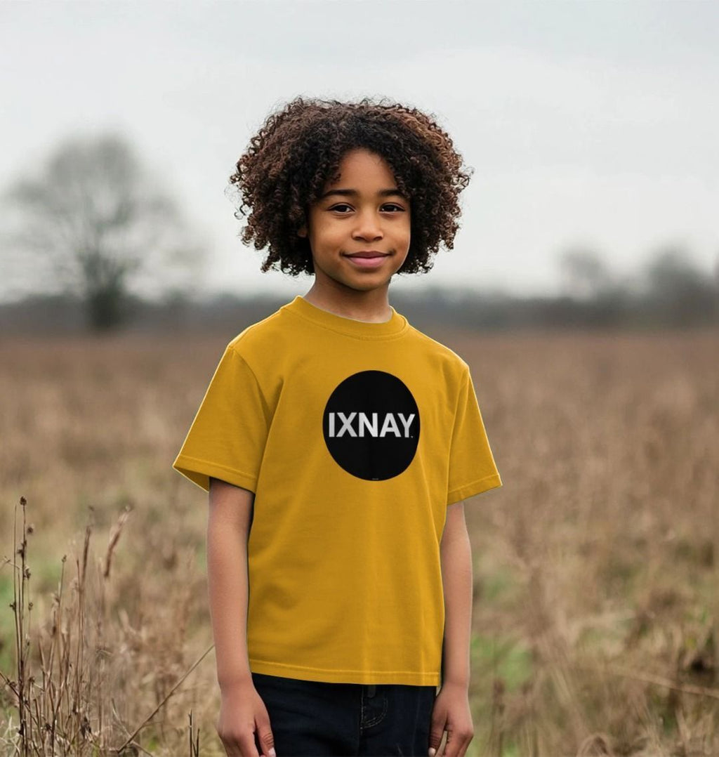 Smiling Black boy with medium length standing in an autumn field wearing a mustard yellow t-shirt with the original IXNAY black circular logo printed on the front