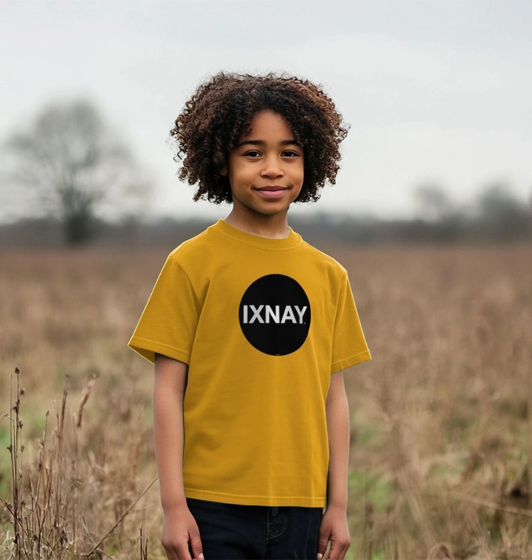Smiling Black boy with medium length standing in an autumn field wearing a mustard yellow t-shirt with the original IXNAY black circular logo printed on the front