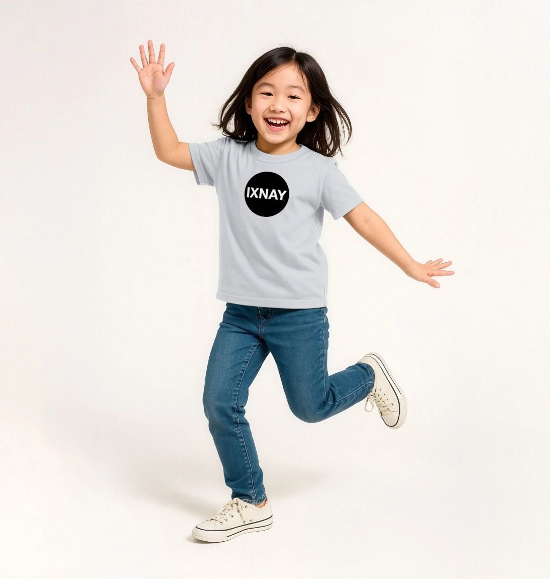 Smiling young Asian girl jumping and waving at the camera during a photoshoot with a solid white background wearing a white t-shirt with the original IXNAY black circular logo printed on the front