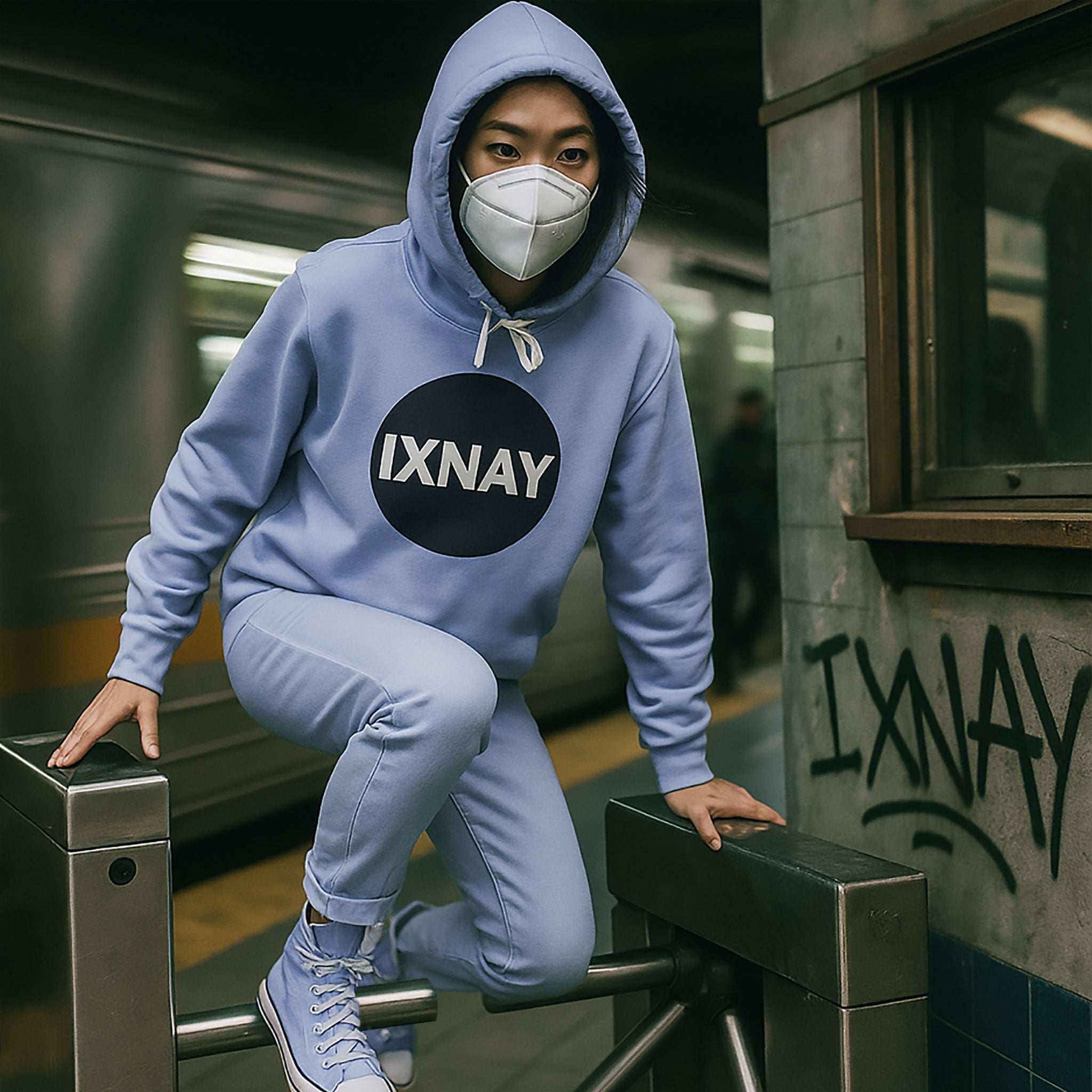 Person wearing a blue women's hoodie with 'IXNAY' logo in a subway setting