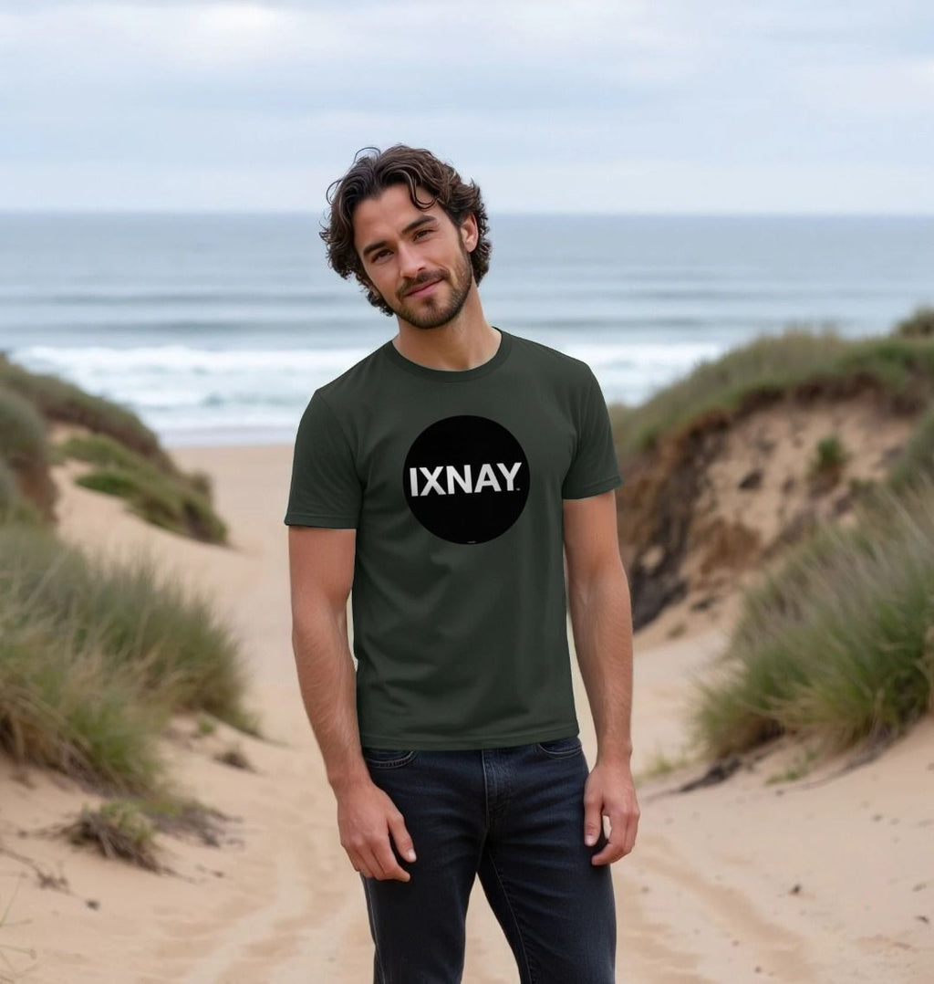 Smiling man standing among grassy dunes on a beach wearing a dark gray Printed Men's T-Shirt with Original Black Round IXNAY Logo with the phrase REJECT REJECTS REJECTOR on back  to represent the artist and musician IXNAY