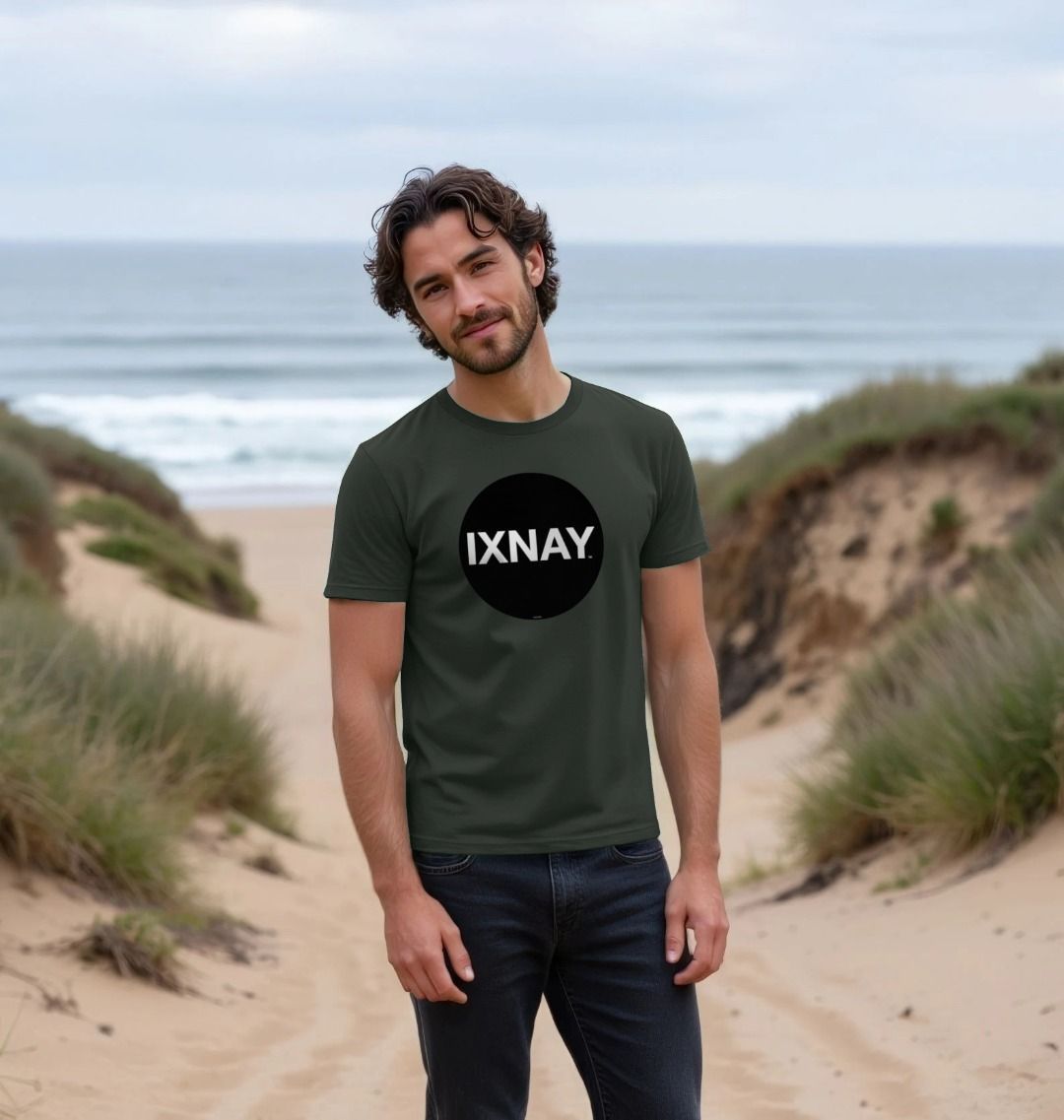 Smiling man standing among grassy dunes on a beach wearing a dark gray Printed Men's T-Shirt with Original Black Round IXNAY Logo with the phrase REJECT REJECTS REJECTOR on back  to represent the artist and musician IXNAY