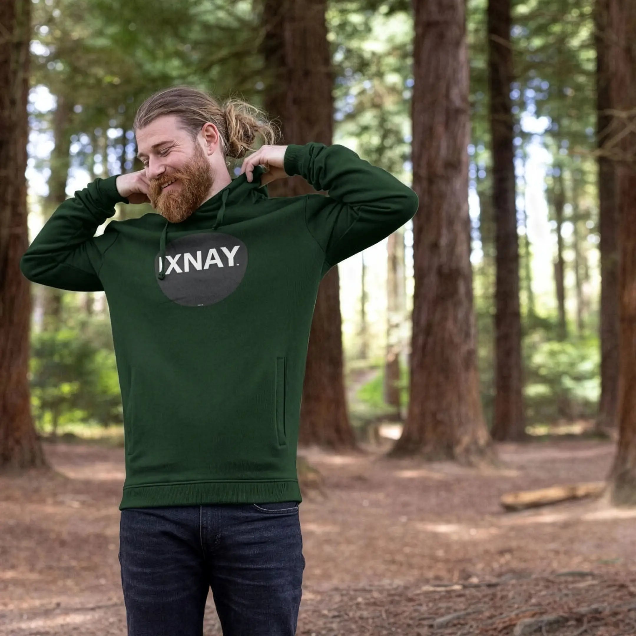 Man walking in woods wearing mens dark green organic cotton pullover hoodie with original black round IXNAY logo.