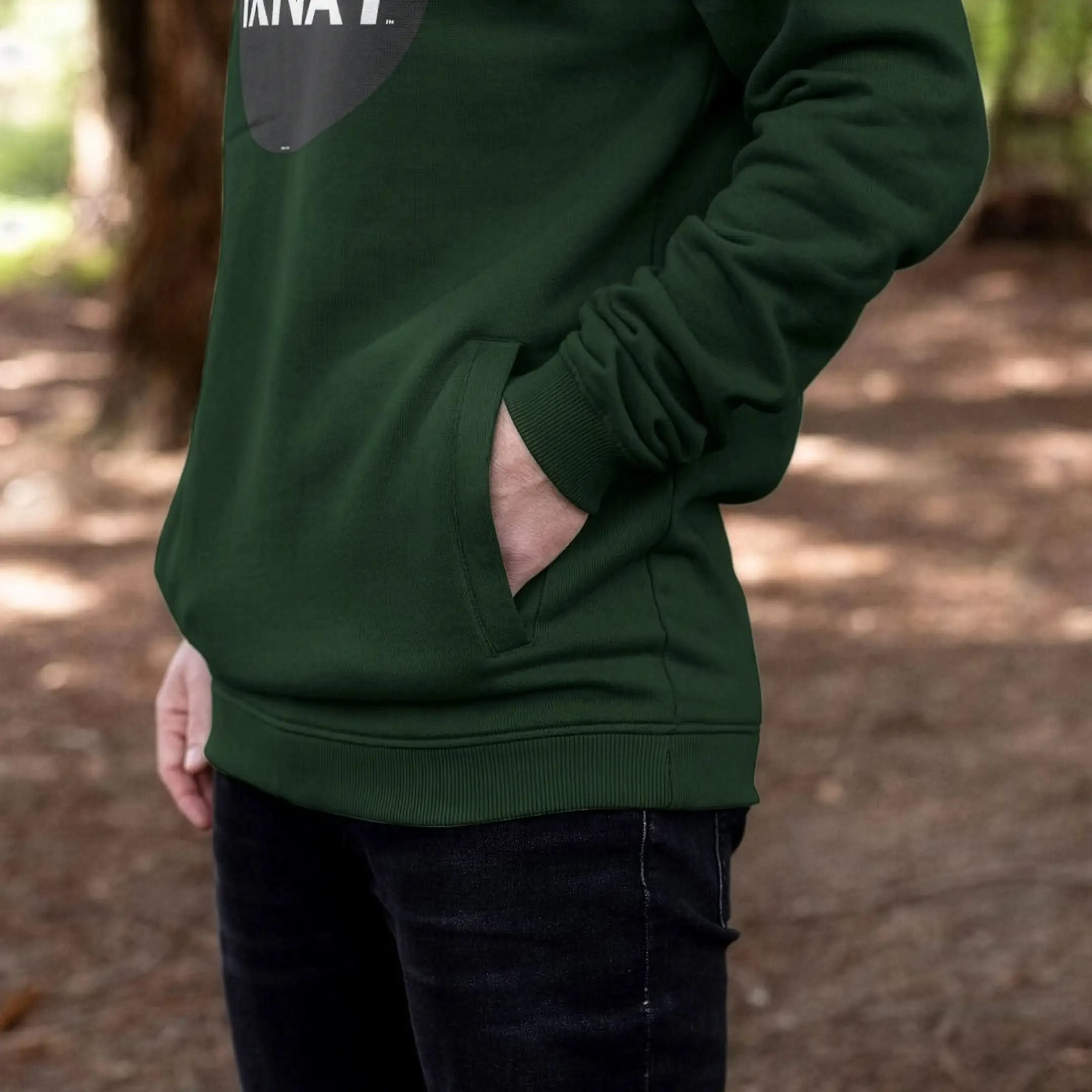 Man wearing mens dark green organic cotton pullover hoodie with original black round IXNAY logo showing side pocket details.