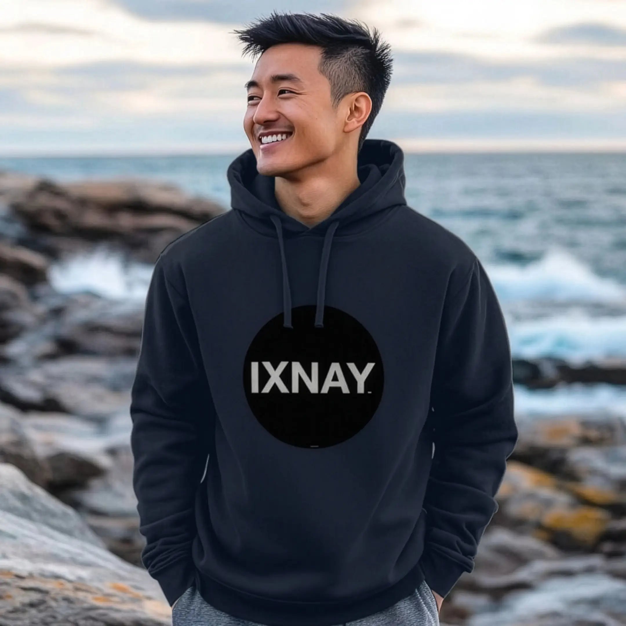 Man walking on rock jetty wearing mens navy blue organic cotton pullover hoodie with original black round IXNAY logo.