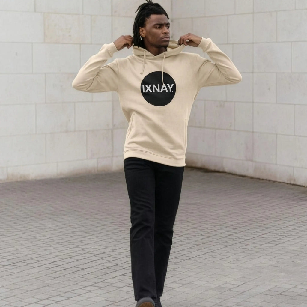 Man in front of white marble wall wearing mens oat light beige organic cotton pullover hoodie with original black round IXNAY logo.