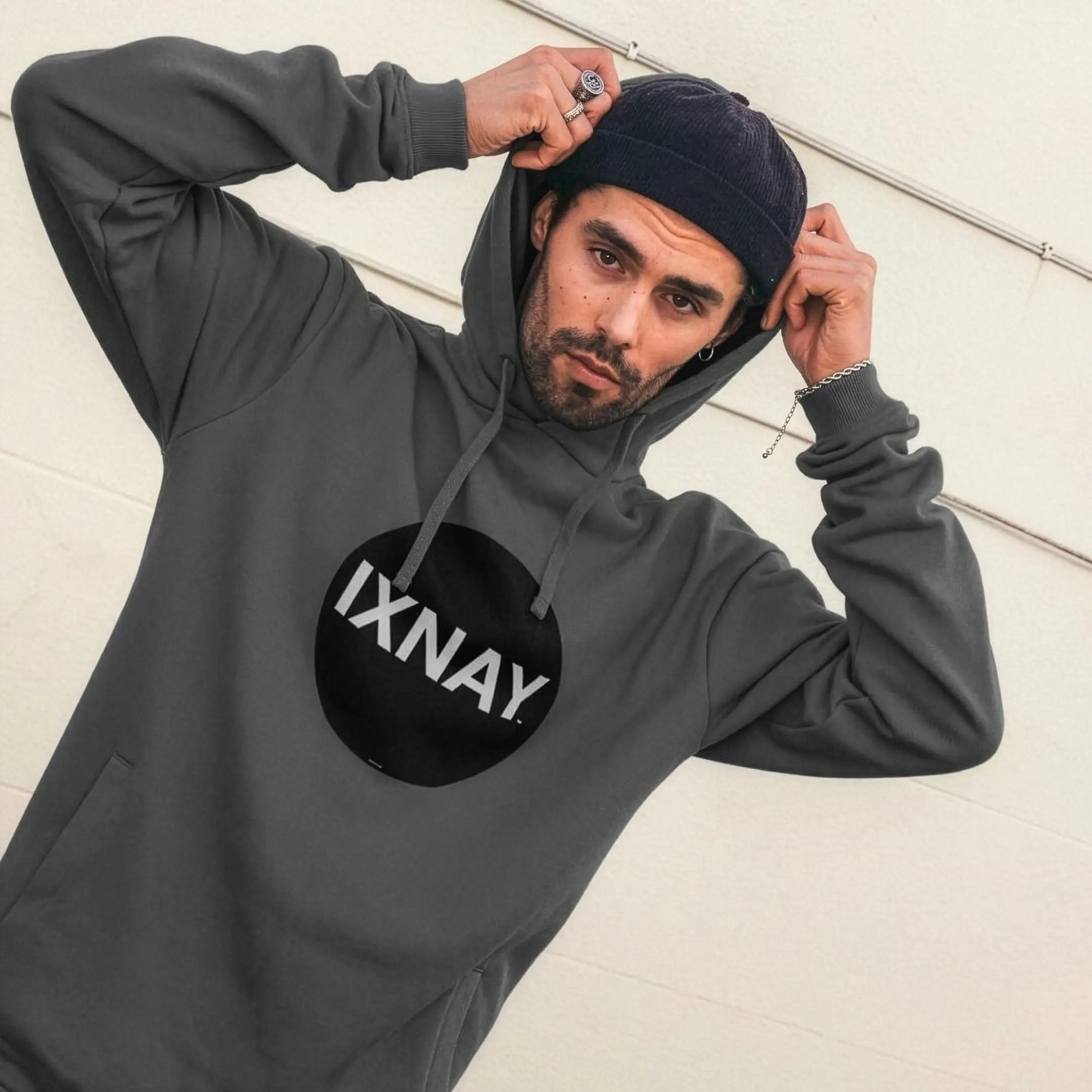 Man pulling up his hood while wearing mens dark slate gray organic cotton pullover hoodie with original black round IXNAY logo.