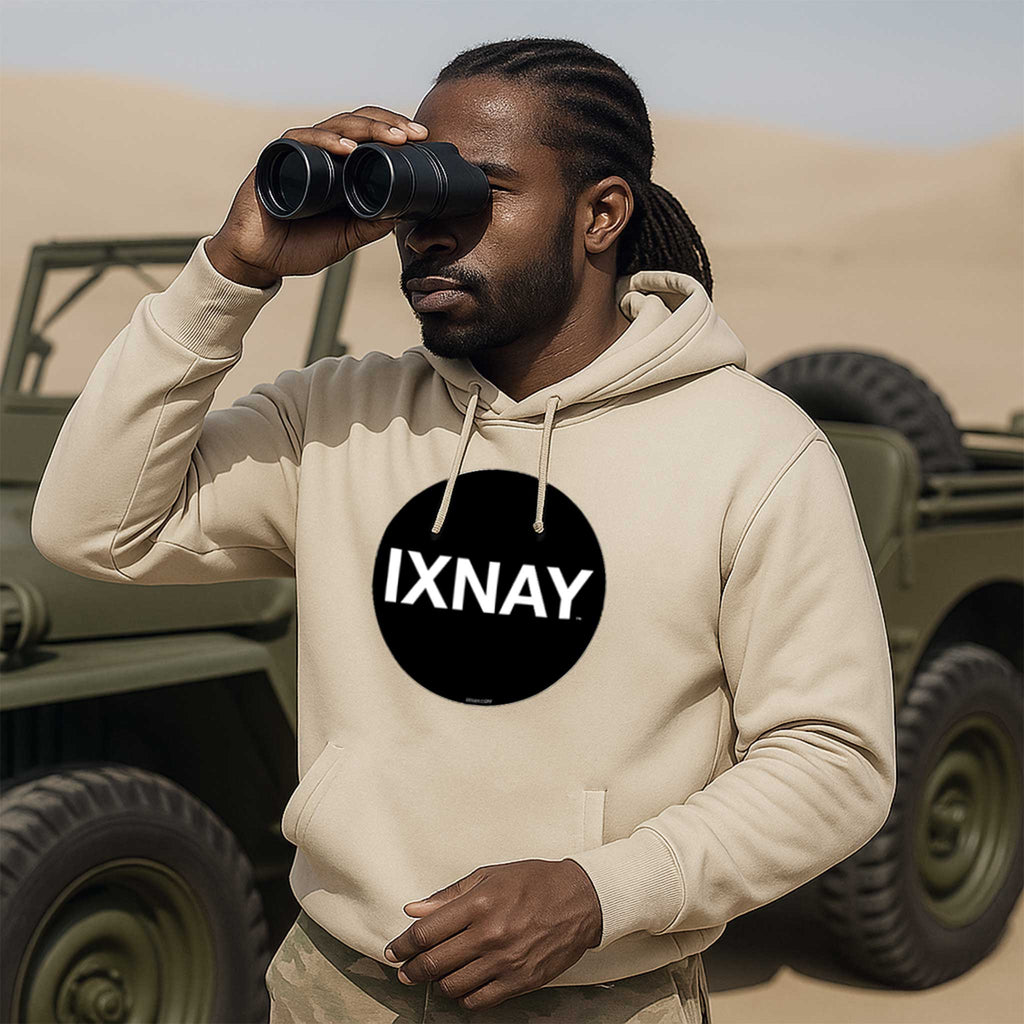 Man wearing a beige hoodie with 'IXNAY' logo, using binoculars in a desert setting with military vehicles.