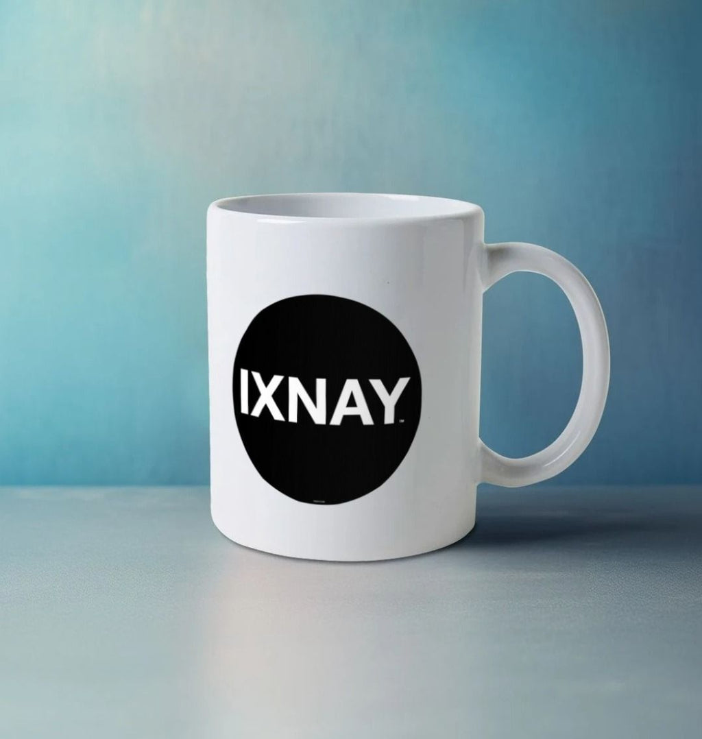 Image shows a white ceramic mug emblazoned with the black logo with white lettering for the artist and musician IXNAY on a marble counter top with a wall painted in a light denim blue wash in the background