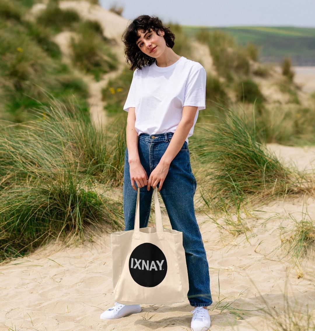 woman at beach holding IXNAY original round logo tote bag natural 100% organic cotton canvas