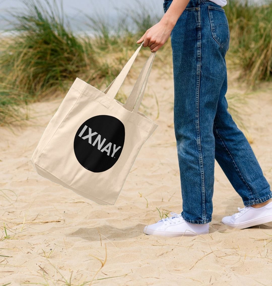 woman at beach swinging by handle the IXNAY original round logo tote bag natural 100% organic cotton canvas