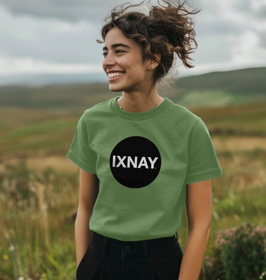 Smiling woman standing in a rolling hill landscape wearing a Sage Green Printed Women's T-Shirt with Original Black Circular IXNAY Logo
