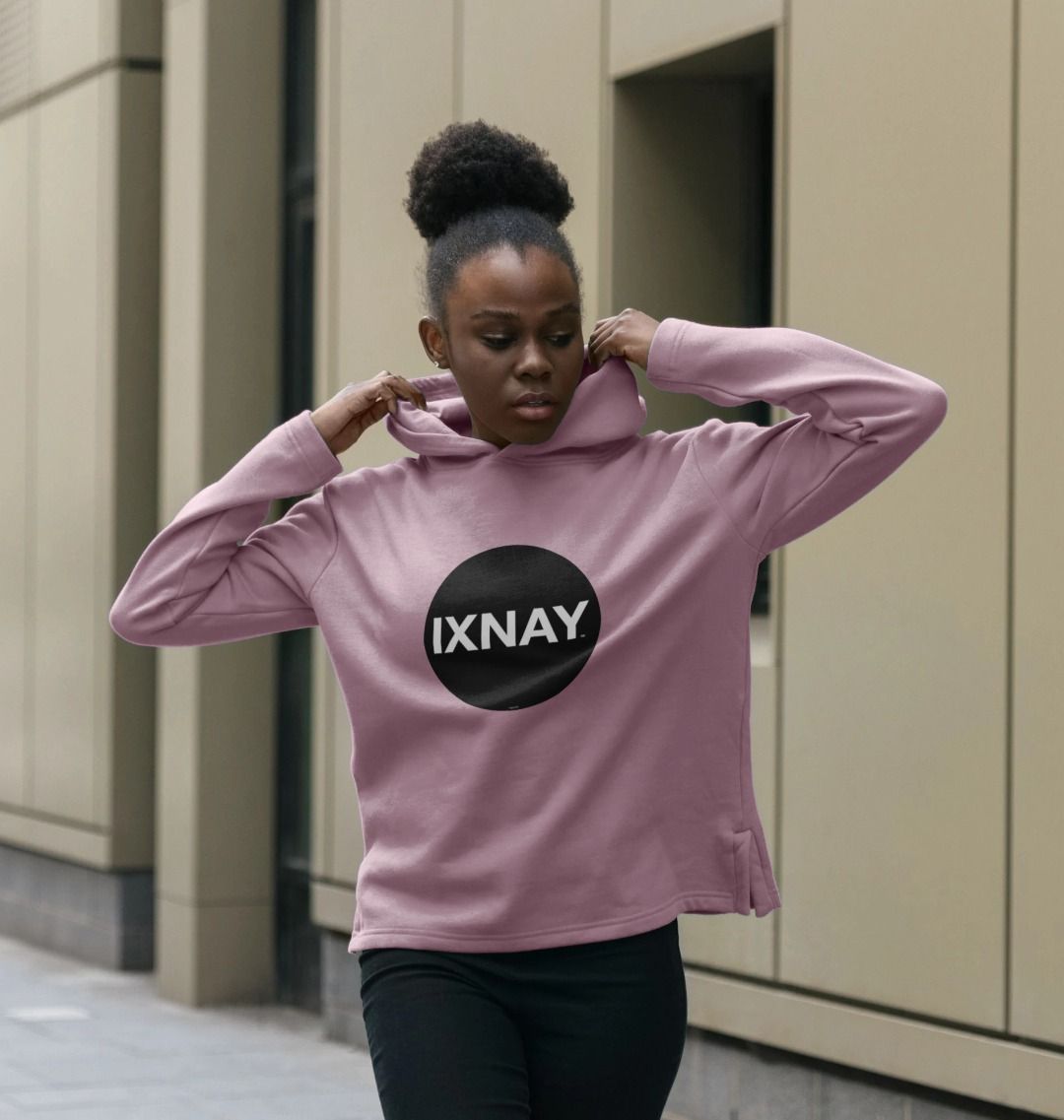 Woman on city street wearing women's mauve pink organic pullover hoodie with original black round IXNAY logo