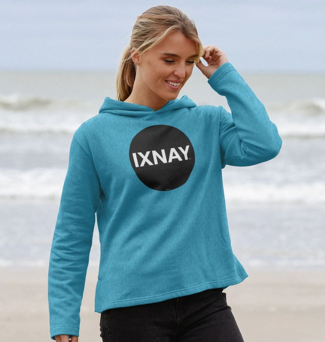 woman on beach near oceans edge wearing womens ocean blue organic remill pullover hoodie with original black round IXNAY logo