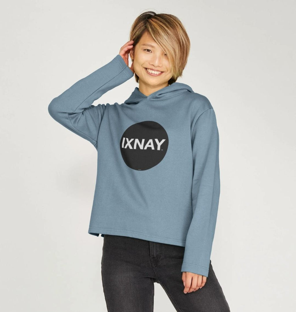 Woman in front of white background wearing women's blue organic pullover hoodie with original black round IXNAY logo