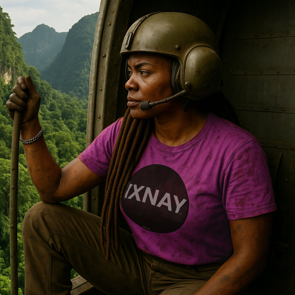 Woman wearing a helmet and pink t-shirt with 'IXNAY' logo, sitting in the open door of a helicopter flying over a mountainous landscape.